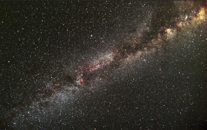 A wide, dense band of the Milky Way galaxy glows with countless bright white stars, dark dust lanes, and luminous nebulae stretching diagonally across a deep night sky. The unlabelled landscape photograph highlights the specific section of the galaxy containing the Kepler space telescope's field of view. Cosmic dust streams cut through the central galactic plane, creating rich visual contrast against the dense star fields behind them.